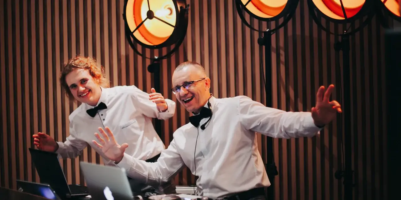 Dwóch DJ-ów w białych koszulach i czarnych muszkach, gotowych do zabawy. Zastanawiasz się, ile kosztuje dj na wesele?