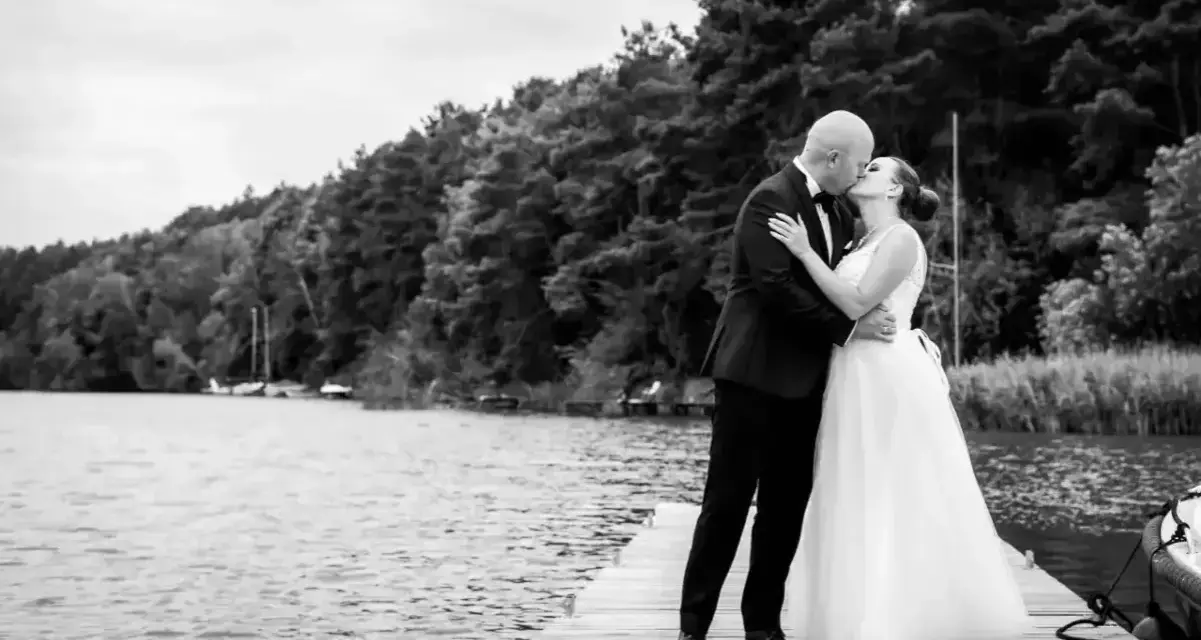 Para młoda całuje się na pomoście. Zastanawiasz się, ile kosztuje fotograf na wesele? Taka sesja to wspaniała pamiątka.