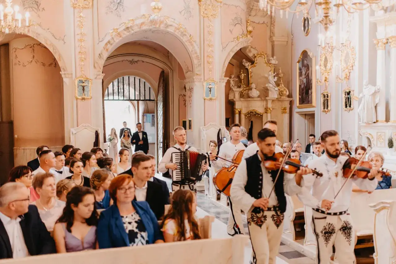 Muzycy grają pieśni na ślub w kościele. W tle para młoda wchodzi do świątyni.