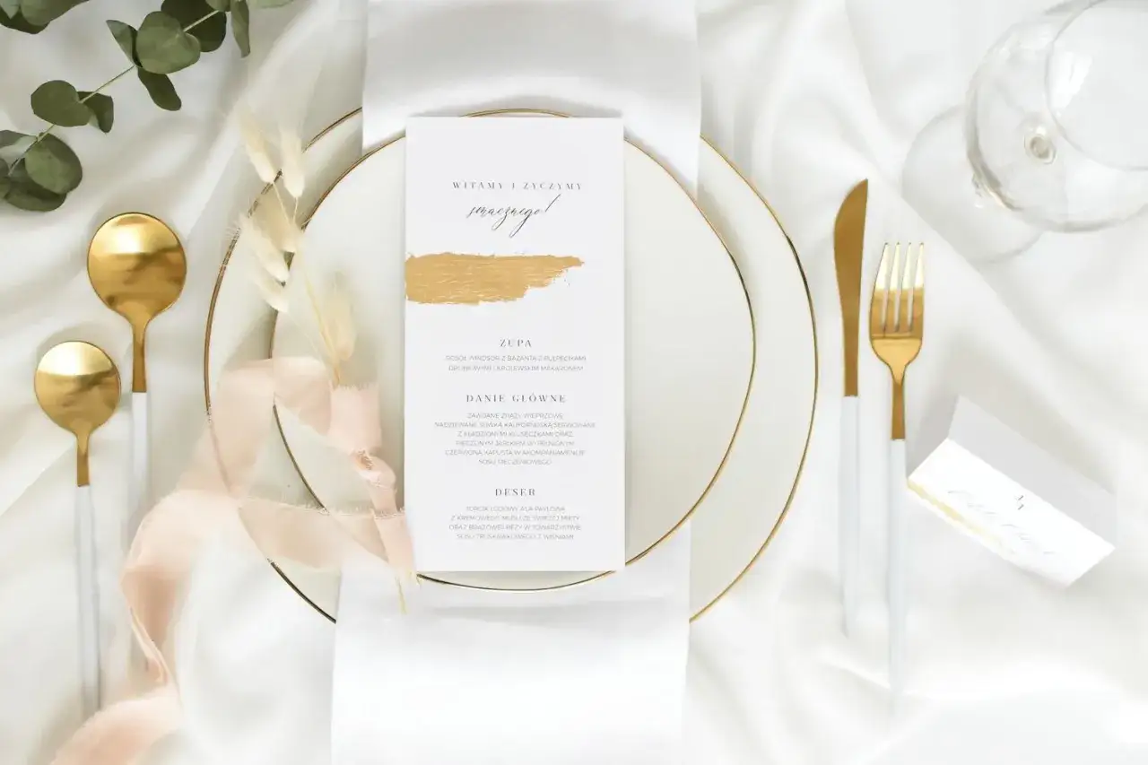Elegancka zastawa stołowa z menu weselnym. Złote sztućce i talerze sugerują, ile kosztuje talerzyk na weselu, tworząc wykwintną atmosferę.